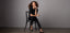 Female model wearing high rise skinny jeans paired with black heels, sitting on a chair in a minimalist setting, showcasing ankle skinny jeans for a sleek, modern look.